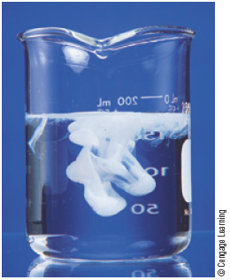 A photo shows a white precipitate forming in a beaker filled upto three-quarters with a clear solution.